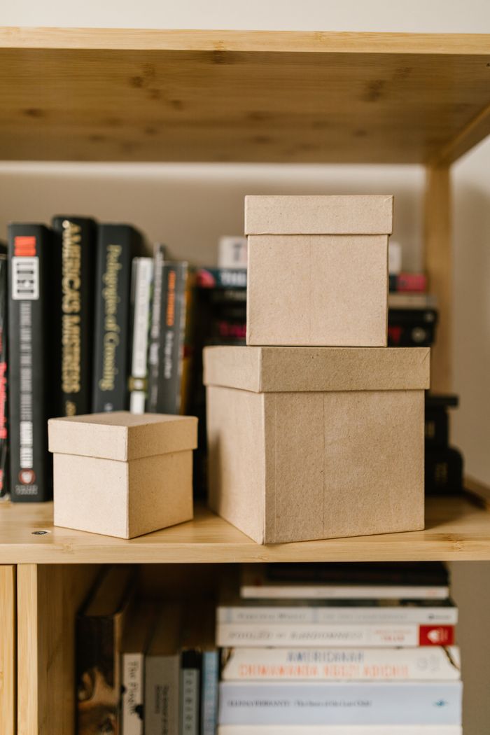 Close-up of cardboard boxes on a wooden bookshelf surrounded by various books.
